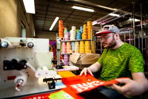 Kirk, wearing a green shirt and a hat, working at a labeling machine at Peace Coffee.