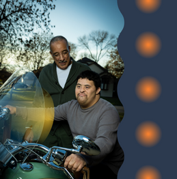 A photo of two men, one standing and one sitting on a motorcyle, with orange and navy blue decorative elements on the right side.